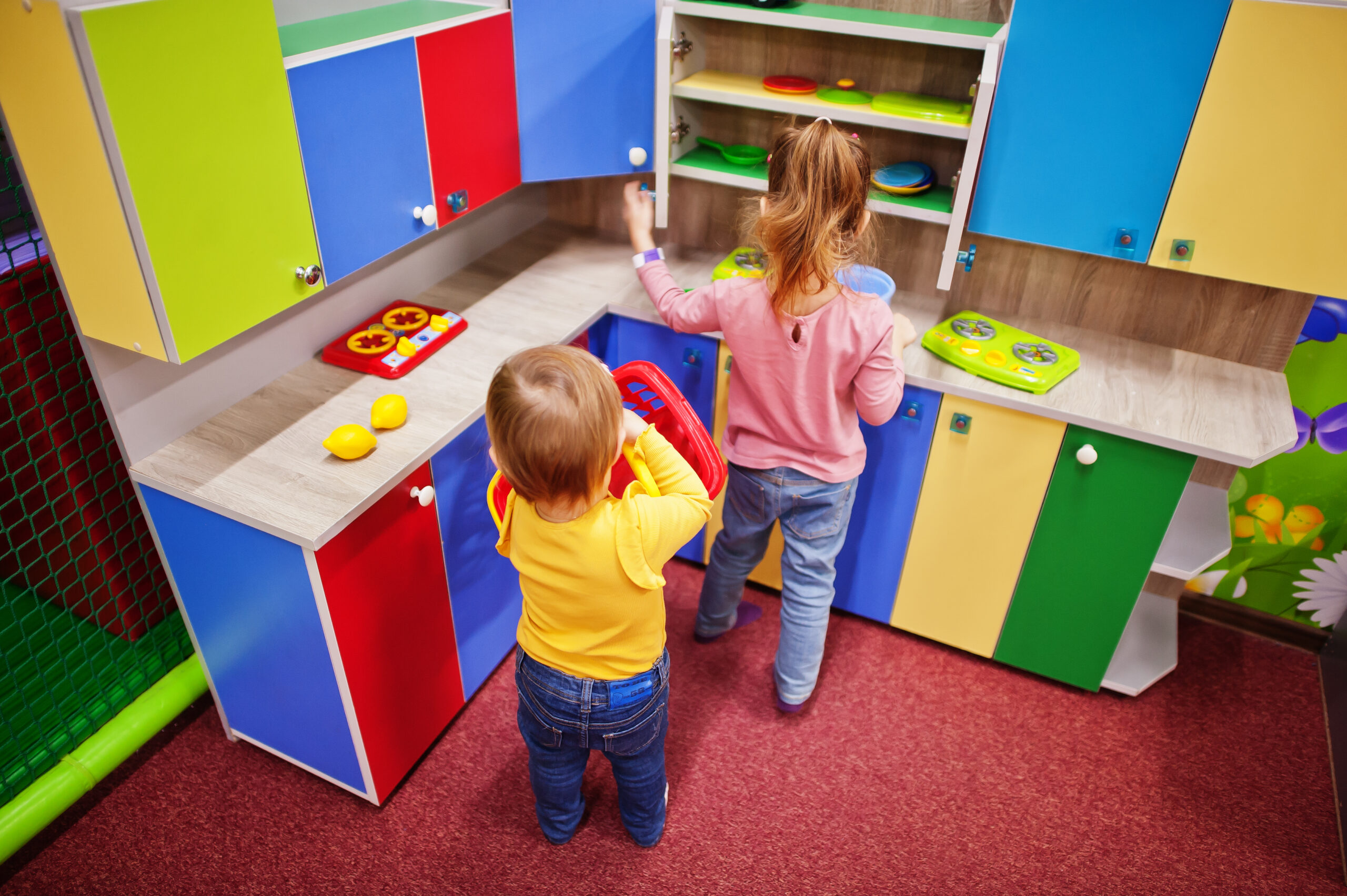 Cute sisters playing in indoor play center. Kindergarten or preschool play room. In the children's kitchen.